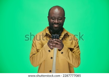 African American man reading a message on his mobile phone and smiling standing against green background