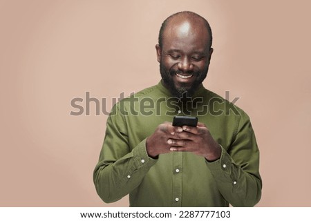 African American man in green shirt reading message on his smartphone and smiling standing on brown background