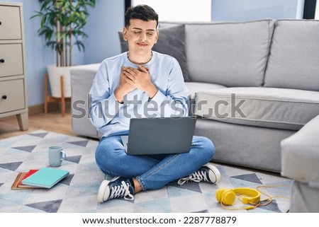 Non binary person studying using computer laptop sitting on the floor smiling with hands on chest with closed eyes and grateful gesture on face. health concept. 