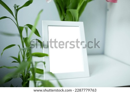 white frame mockup with plants and tulip flowers on white and grey background.