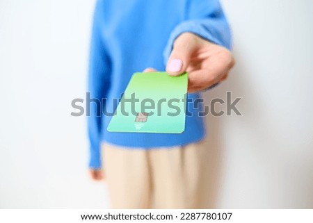 Unrecognizable female holds out her green gradient credit card to make an electronic payment. Modern female doing a cashless transaction using the contactless tap-to-pay method on grey backdrop. NFC.