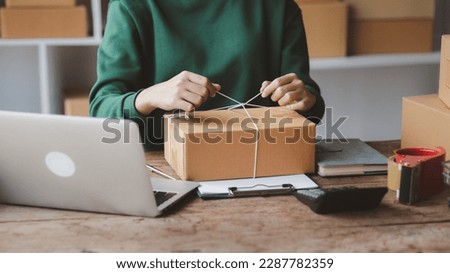 An woman tying a parcel to a customer's box, she owns an online store, she packs and ships through a private transport company. Online selling and online shopping concepts. Royalty-Free Stock Photo #2287782359