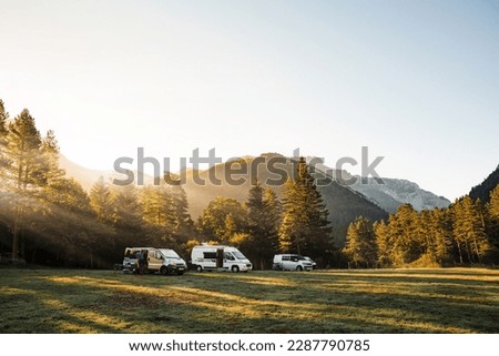 Camper vans in a valley with amazing landscape views of forest, mountains and sun rays during sunrise. Van road trip holiday and outdoor summer adventure. Nomad lifestyle concept Royalty-Free Stock Photo #2287790785