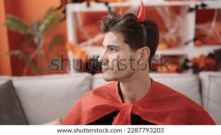 Young hispanic man wearing devil costume having halloween party at home