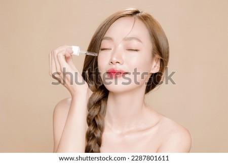 Young Asian woman long hair braid with natural makeup on face and clean fresh skin using dropper to apply serum on isolated beige background. Female model in studio. Facial treatment, Cosmetology.