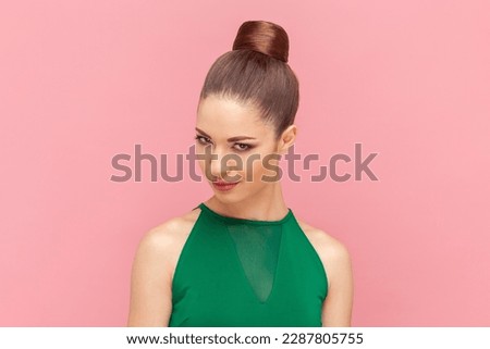 Portrait of cunning woman with bun hairstyle looking at camera with sly facial expression, having devil plant or preparing prank, wearing green dress. Indoor studio shot isolated on pink background. Royalty-Free Stock Photo #2287805755