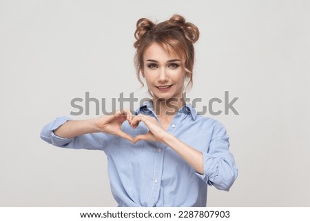 Be my valenetine. Portrait of blonde woman confesses in love, showing heart gesture, having romantic feelings, feels passion, wearing blue shirt. Indoor studio shot isolated on gray background.