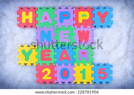 Happy New Year 2015 sign made out of alphabet and numbers puzzle pieces isolated on icy background