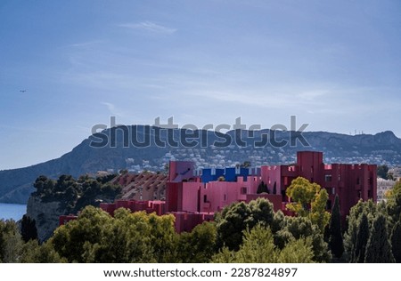 Red Wall Building Built by the Architect Ricardo Bofill on the Coast of the City of Calpe Seen from a Far Hidden Behind the Trees with the Sea in the Background