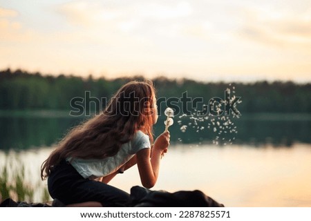 Pretty  little girl  is smiling in the park with dandelion flower. Happy cute kid having fun outdoors at sunset. Royalty-Free Stock Photo #2287825571