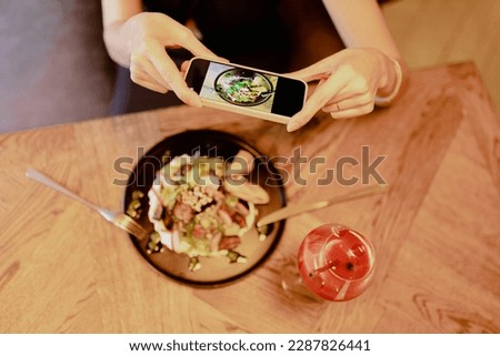Woman photographs plate with institution 's signature dish while sitting in restaurant. Enjoying taste. Recreation and entertainment. Delicious food. Specialty of establishment. Blogger. 