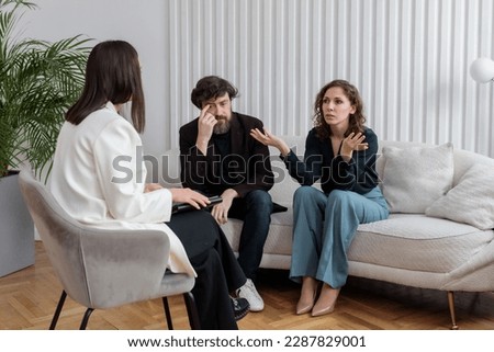 Concept of marital therapy. A female psychologist sits with her back to the camera and listens to the quarrel of a married couple during a therapy session Royalty-Free Stock Photo #2287829001
