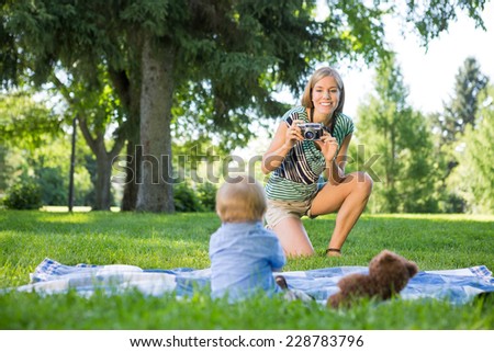 Smiling mid adult mother taking picture of baby boy in park