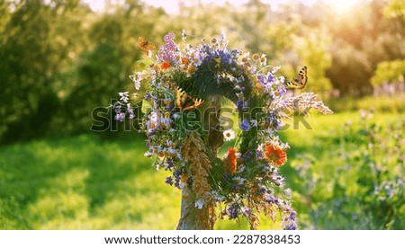flowers wreath on wooden post and butterflies on sunny meadow natural background. Floral crown, symbol of Summer Solstice Day, Midsummer holiday. witch tradition, wiccan ritual. Litha sabbat. Royalty-Free Stock Photo #2287838453