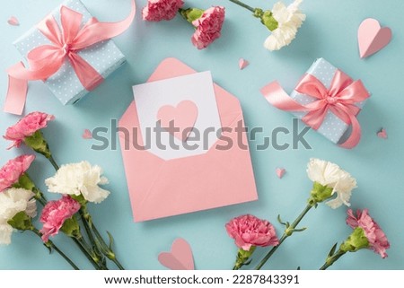 Mother's Day sentiment concept. Top view flat lay photo of postcard, gift boxes with pink ribbons, carnation flowers, and pink paper hearts on pastel blue background