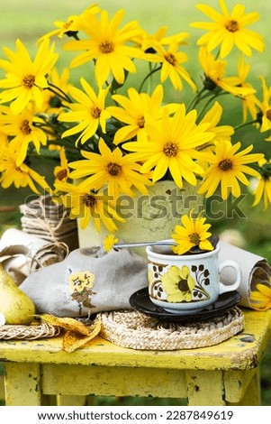 Blooming Jerusalem artichokes plant flowers in vase, in nature background, still life with  flowering Jerusalem artishokes on yellow table Royalty-Free Stock Photo #2287849619