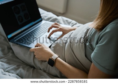 Millennial female freelancer lying in bed and using laptop. Woman work from home. Comfortable workplace.