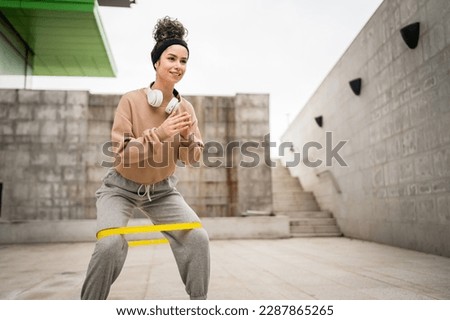 One woman adult caucasian female athlete training with elastic rubber resistance bands in outdoor in the city on concrete background stretching in happy brunette health and fitness concept copy space