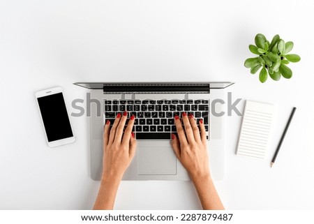 Overhead shot of female hands using laptop on white office desktop. Business background. Flat lay
