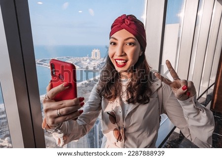 Indian girl travel blogger taking selfie photos on her smartphone from height of a rooftop viewpoint on skyscraper in Abu Dhabi, UAE