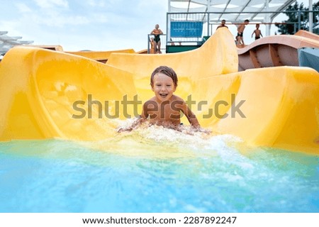 Cheerful blue-eyed kid on a water slide in the water park, a little boy merrily slides into the water along the slide in the amusement park, rest with children in the water park Royalty-Free Stock Photo #2287892247
