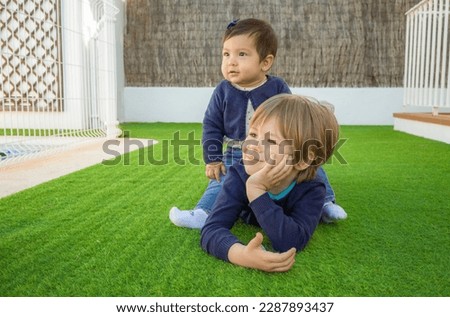 Picture of brother and sister having fun in the park, two cheerful children laying down on green grass, little girl and boy playing outdoors, best friends, happy family, love and happiness concept