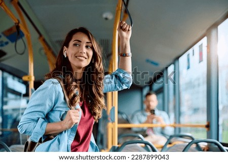 Young smiling woman holding onto a handle while traveling by public bus. Royalty-Free Stock Photo #2287899043