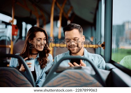 Young happy mand and his girlfriend using cell phone while traveling by public transport. Royalty-Free Stock Photo #2287899063