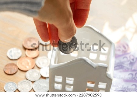 Close-up of hand putting a coin in ceramic house piggy bank. High quality photo
