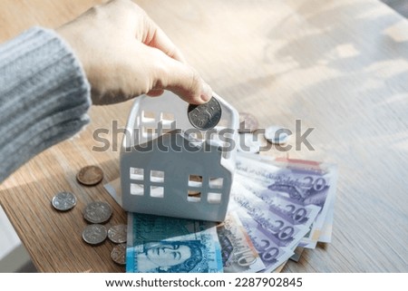 A hand putting a coin in ceramic house piggy bank. High quality photo