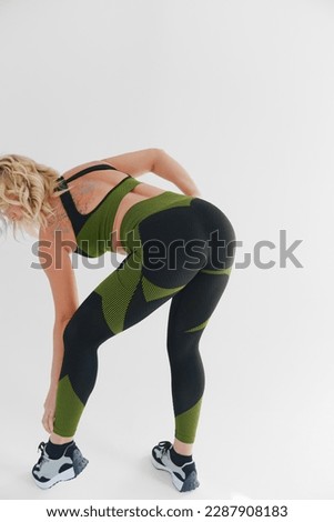 rear view. an attractive blonde in a tracksuit makes inclines on a white background. the concept of a photo shoot for a trainer and advertising in social networks. fitness clothes. sports buttocks
