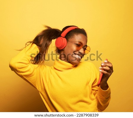 Young afro american female with dances in rhythm of melody. Portrait woman with headphones over yellow color background.