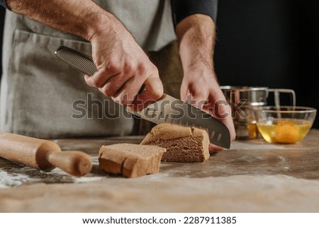 Unrecognizable man cutting the dough with a knife on a wooden background. Close-up of male hands preparing homemade noodles. Selective focus.