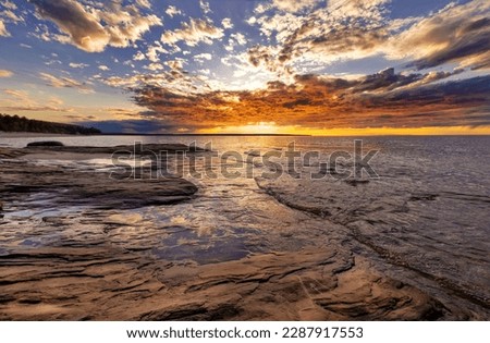 Dramatic sunset over Lake Superior with colorful clouds and a dramatic, rugged shore. Sunset reflections on the surface of the Great Lake show off the coast of Pictured Rocks near Munising Michigan.