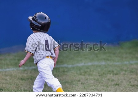 View of a tee ball player running on the field. Small child playing T-ball.
