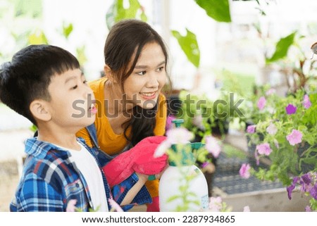 Happy Asian woman and little boy planting a house plants in green house together. Satisfied little boy enjoy planting and watering a small tree with his mother in greenhouse.