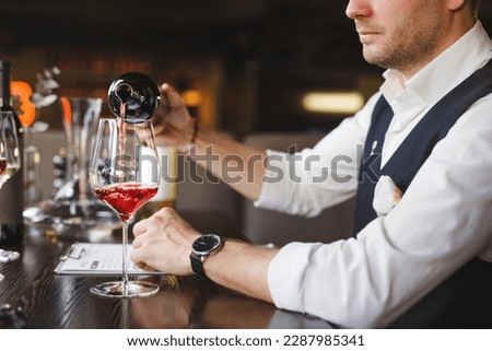 Faceless sommelier pours red wine into stem glass. Royalty-Free Stock Photo #2287985341