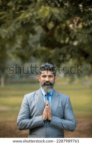Indian businessman giving namaste or welcome gesture at park.