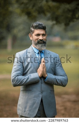 Indian businessman giving namaste or welcome gesture at park.