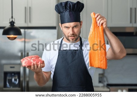 Man chef cooker hold fish and meat, salmon and beef. Male chef in chefs uniform with raw meat beef and fish salmon fillet. Chef man cooking raw meat beef and fish salmon fillet on kitchen.