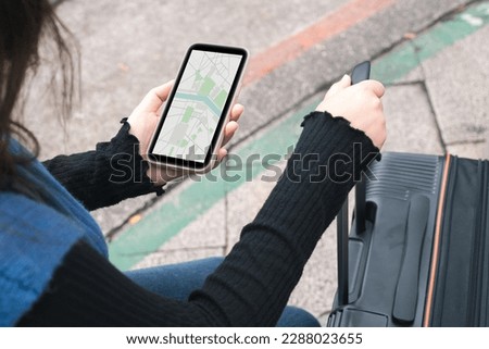 Woman with baggage in downtown city street searching location in map application online on smart phone using GPS navigating