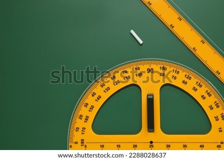 Protractor, ruler and chalk on green chalkboard, flat lay. Space for text