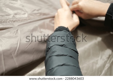 a woman putting up a brown tent with a puffer jacket and a gold ring on her finger at the camping site