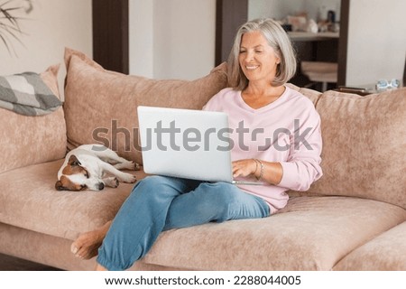 Smiling middle aged woman sit on couch in living room talk on video call on modern laptop, happy excited senior female greeting speak on web using laptop, technology concept   Royalty-Free Stock Photo #2288044005