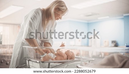 Mother Putting Down a Newborn Child on a Hospital Bassinet Bed in a Modern Nursery Clinic. Caring Mom Comforting Her New Born Child. Healthcare, Pregnancy and Motherhood Concept Royalty-Free Stock Photo #2288052679
