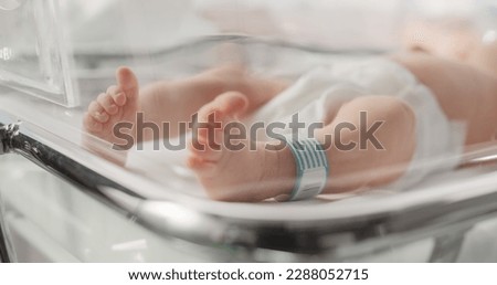 Cute Little Caucasian Newborn Baby Lying in Bassinet in a Maternity Hospital. Portrait of a Tiny Playful and Energetic Child with a Name ID Tag on the Leg. Healthcare, Pregnancy and Motherhood Concept Royalty-Free Stock Photo #2288052715