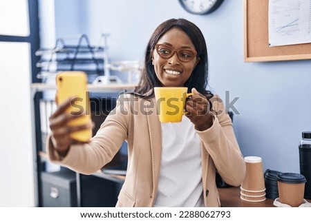 Young african american woman business worker make selfie by the smartphone drinking coffee at office