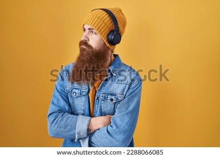 Caucasian man with long beard listening to music using headphones looking to the side with arms crossed convinced and confident 