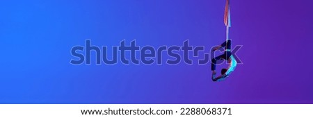 Artistic young man, aerial gymnast, acrobat training with aerial tissue against gradient blue purple background in neon light. Concept of art, sportive lifestyle, motion. Banner. Copy space for ad