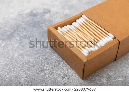 Cotton swabs in craft packaging and holder on a gray cement background. Bamboo cotton buds. Means for hygiene of ears. Eco-friendly materials.Hygienic cotton ear buds.